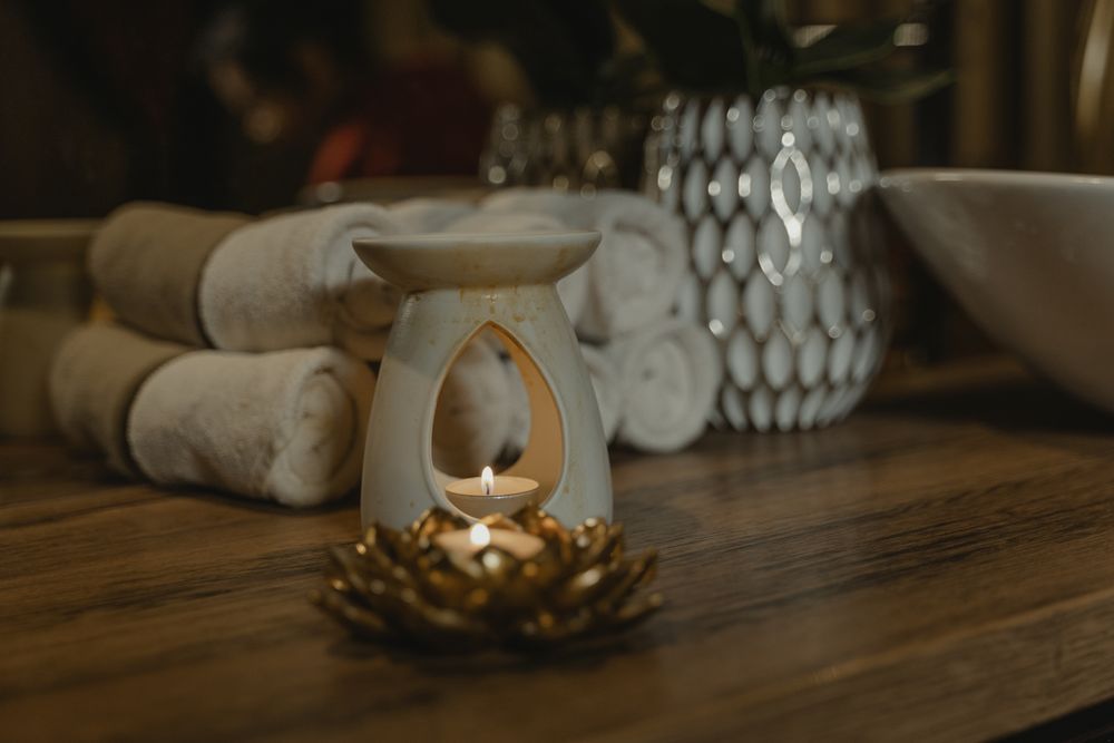 Rolled towels and a lit aromatherapy burner on a wooden table